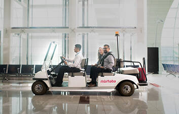 A man and woman being driven through the airport on a marhaba buggy